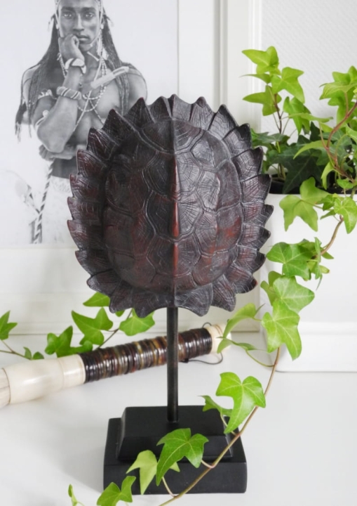 Egzotyczna figurka skorupa żółwia na postumencie stojąca na białym blacie. W tle oprawione czarno-białe zdjęcie etniczne i zielone liście bluszczu