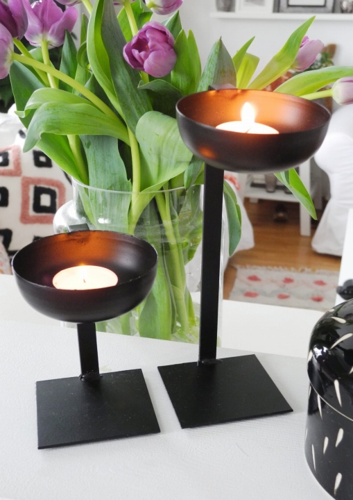 Zestaw 2 czarnych metalowych świeczników na tealight o różnej wysokości, z zapalonymi świeczkami na białej komodzie