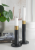 Nowoczesny komplet dwóch czarnych świeczników o rożnych wysokościach na komodzie obok pojemnikó Bloomingville i książki