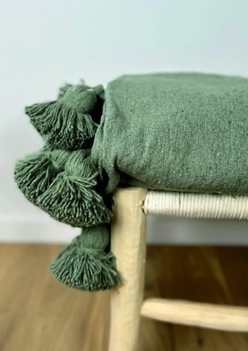 Zielony bawełniany pled z dużymi pomponami na drewnianej ławce w stylu boho