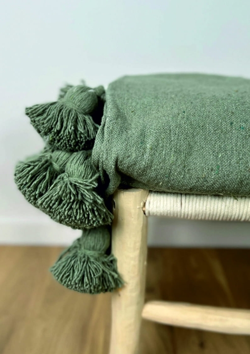 Zielony bawełniany pled z dużymi pomponami na drewnianej ławce w stylu boho