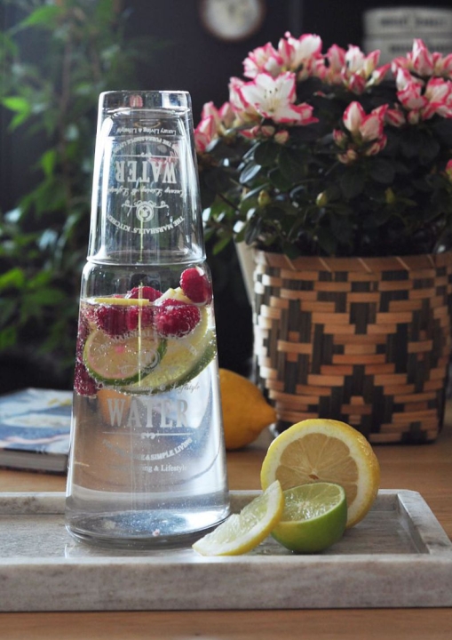 Szklana karafka na wodę ze szklanką wypełniona wodą z malinami i limonką