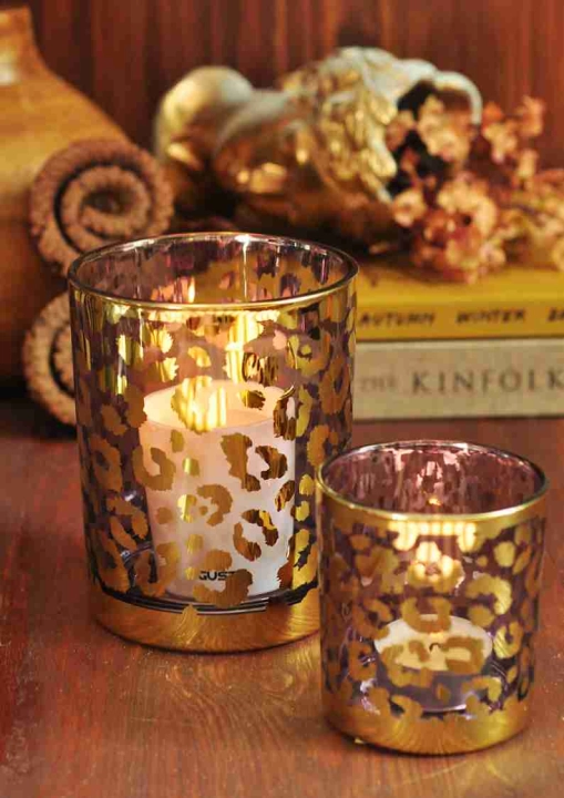 Zestaw szklanych lampionów w złote lamparcie cętki z zapalonymi świecami na drewnianym stole