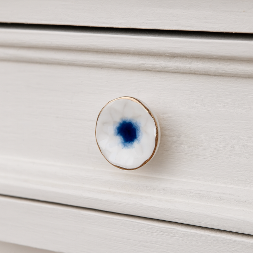 Biało-niebieska ceramiczna gałka meblowa ze złotym rantem zamontowana na białej szufladzie