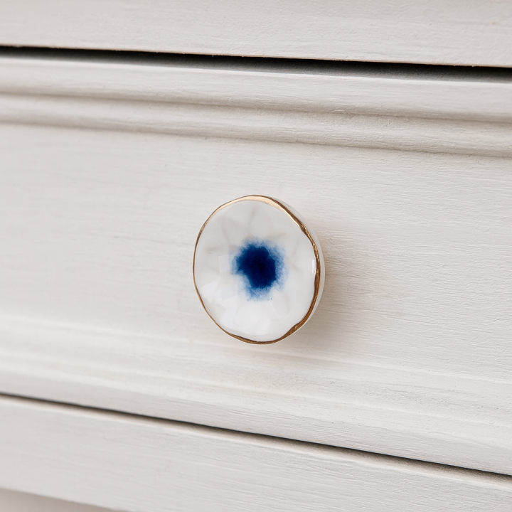 Biało-niebieska ceramiczna gałka meblowa ze złotym rantem zamontowana na białej szufladzie