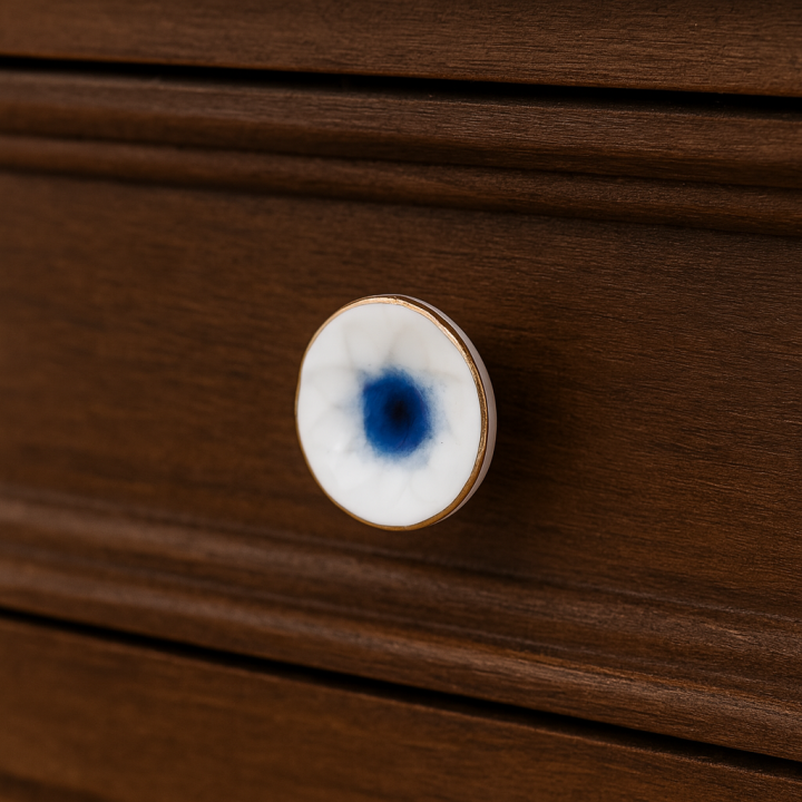 Ceramiczna gałka do mebli w kolorze biało-niebieskim z motywem kwiatka na ciemnym drewnianym froncie szuflady