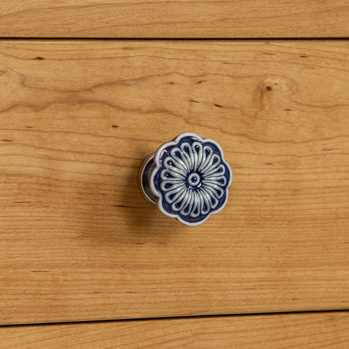 Niebieska ceramiczna gałka meblowa w kształcie kwiatka zamontowana na szufladzie z jasnego drewna