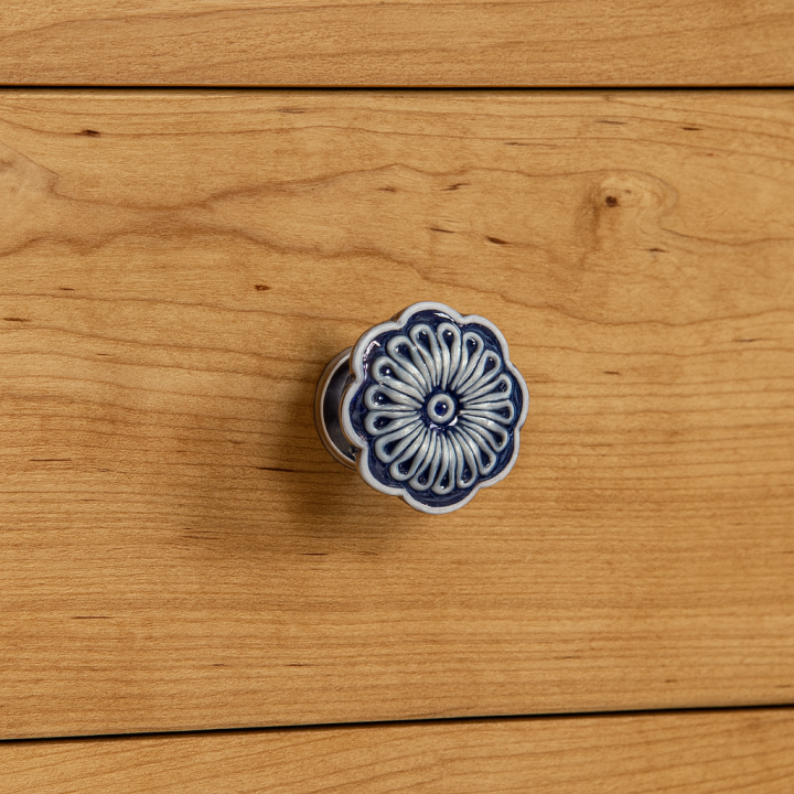 Niebieska ceramiczna gałka meblowa w kształcie kwiatka zamontowana na szufladzie z jasnego drewna