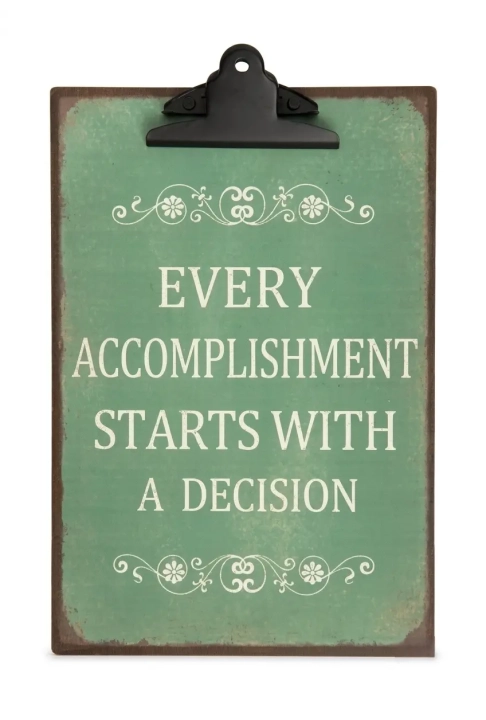 Ciemnozielona, metalowa podkładka z czarnym klipsem w stylu vintage, format A4, z białym ozdobnym tekstem po angielsku: Every accomplishment starts with a decision