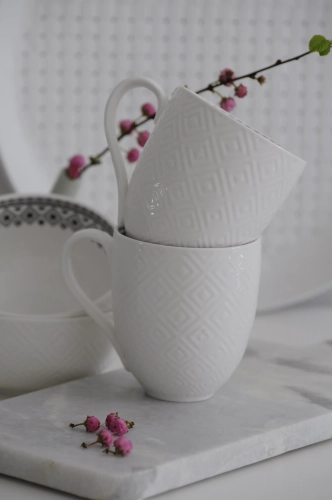 Biały kubek porcelanowy Diamond z wytłaczanym wzorem w romby na zewnątrz i czarnym geometrycznym dekorem wewnątrz, ustawiony na marmurowej desce kuchennej