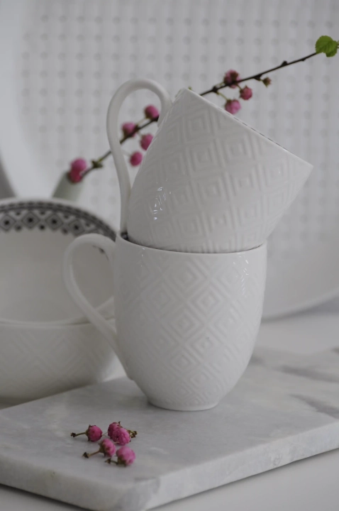 Biały kubek porcelanowy Diamond z wytłaczanym wzorem w romby na zewnątrz i czarnym geometrycznym dekorem wewnątrz, ustawiony na marmurowej desce kuchennej
