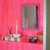 Różowe lustro z falistą ramą w stylu dopamine decor na półce przy neonowej różowej ścianie