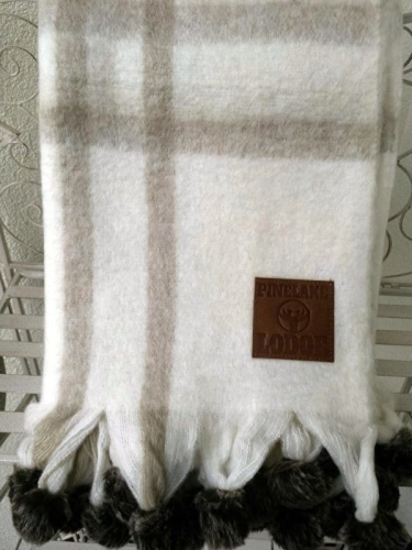 Beżowy koc z domieszką wełny z ozdobnymi pomponami z ekologicznego futerka.